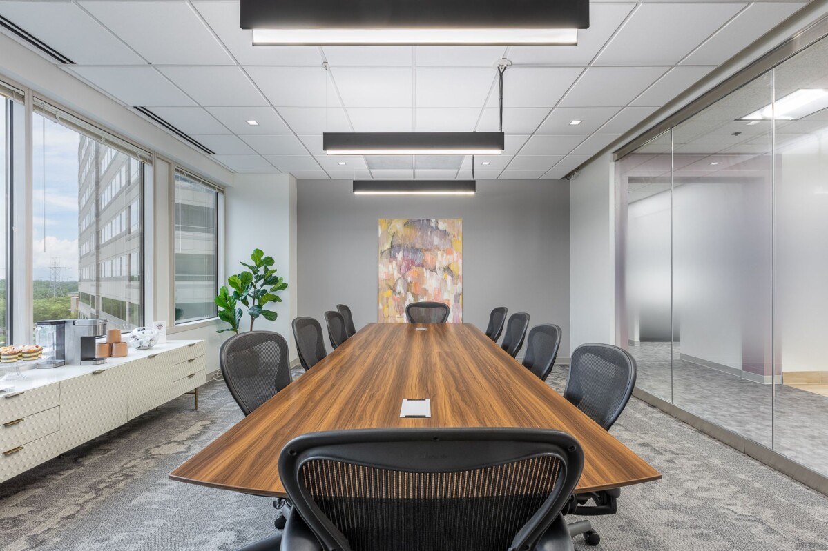 ?seraph accel gi=wp content%2Fuploads%2F2024%2F07%2F004 LC2 - Metro Offices A modern conference room with a long wooden table, black chairs, large windows on the left, abstract wall art, a potted plant, a sideboard with snacks and a glass partition on the right.
