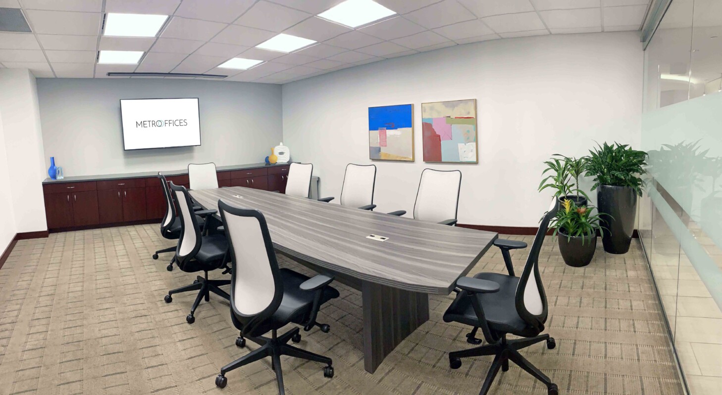 ?seraph accel gi=wp content%2Fuploads%2F2024%2F07%2F007 LC - Metro Offices A modern conference room with a long table, eight chairs, a screen displaying 'METRO FACES,' and wall art. The room has carpeting, an indoor plant, and concealed lighting.