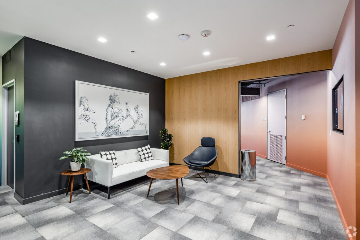 Modern waiting area in an office space in Chevy Chase with a white sofa, round wooden table, black chair, and abstract wall art. The room features two-tone walls and a plant near the sofa.