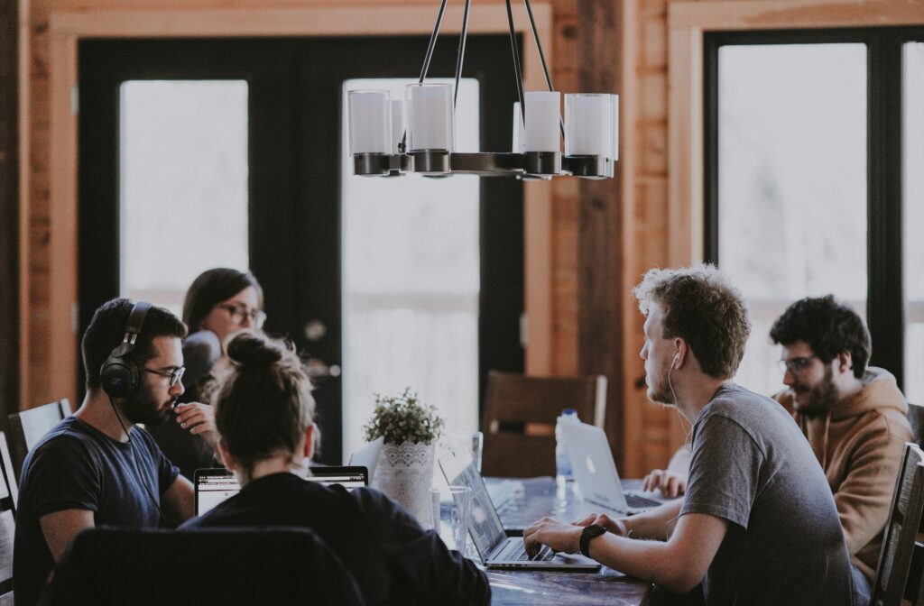 A group of people working together in a coworking space, sitting around a table with laptops.