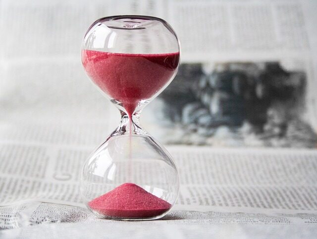 A glass hourglass with red sand stands on a newspaper, symbolizing the future of work as sand falls from the upper to lower chamber—perfect for growing businesses seeking innovative virtual office space solutions.