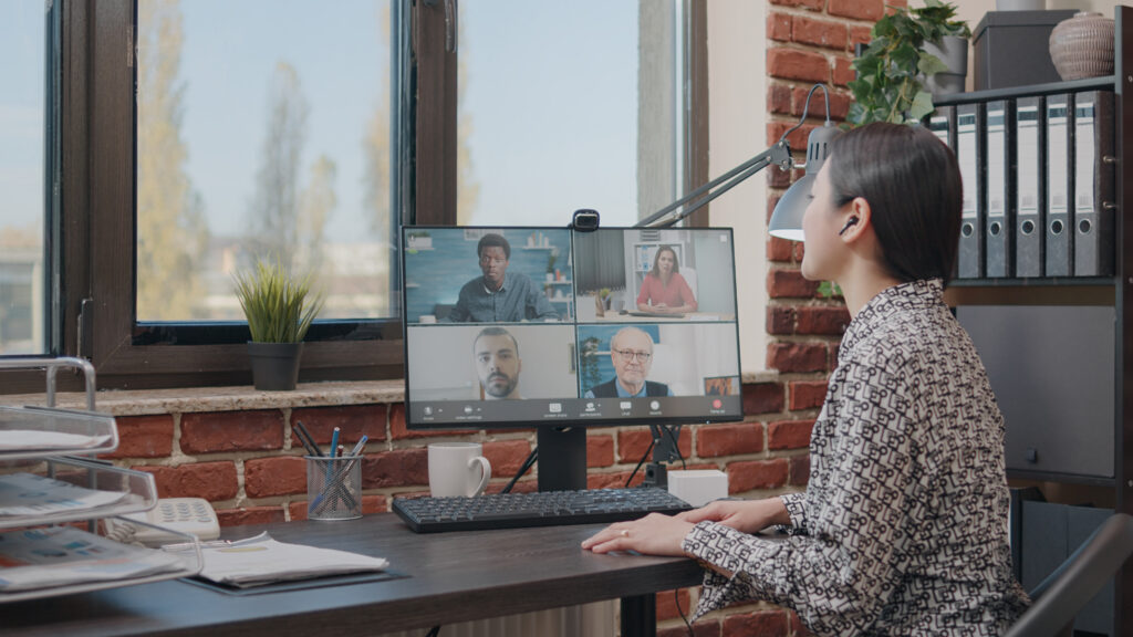 business woman talking colleagues online video call doing teamwork project planning person using remote video conference have conversation about development teleconference - Metro Offices A woman is sitting at a desk in a virtual office.