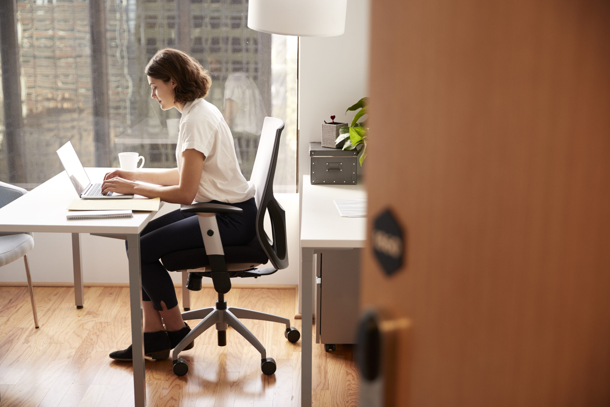 businesswoman sitting desk working laptop modern office viewed through door way scaled - Metro Offices What Is a Virtual Office Address and Its Benefit for Businesses? | Metro Offices