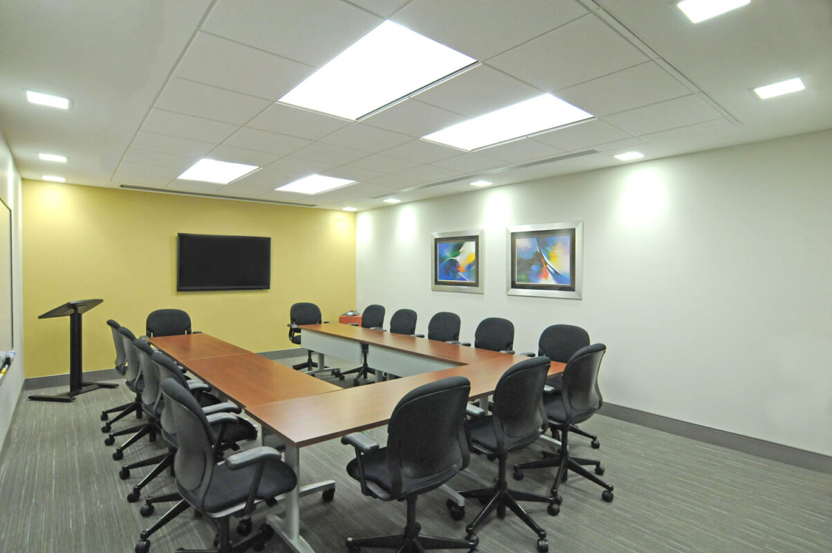 ?seraph accel gi=wp content%2Fuploads%2F2024%2F07%2F002 T - Metro Offices A conference room with a long rectangular table, several black office chairs, a podium, a wall-mounted TV, and two pieces of framed artwork on the wall.