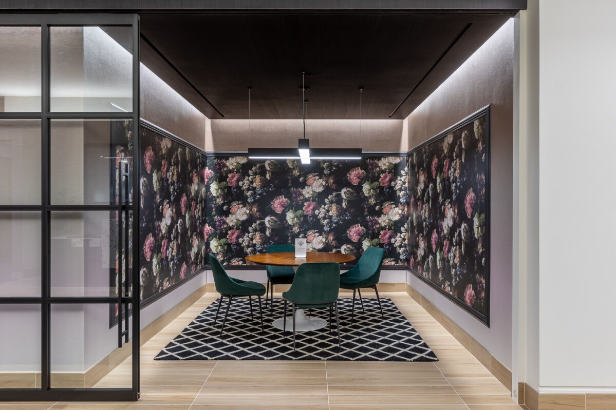 ?seraph accel gi=wp content%2Fuploads%2F2024%2F07%2F004 FD - Metro Offices Modern meeting room with a round wooden table, four green chairs, and floral wallpaper. The room has a geometric rug and is enclosed by glass walls.