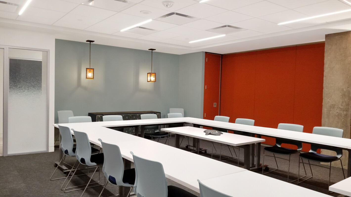 ?seraph accel gi=wp content%2Fuploads%2F2024%2F07%2F005 TR - Metro Offices A modern conference room with U-shaped white tables, light blue chairs, red accent wall, and frosted glass door. Two ceiling lights illuminate the room.