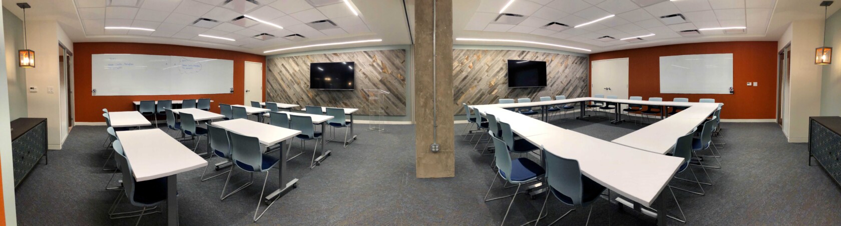 ?seraph accel gi=wp content%2Fuploads%2F2024%2F07%2F005 TR2 - Metro Offices Panoramic view of a modern classroom featuring desks, chairs, whiteboards, and large monitors on the walls. The room is brightly lit with overhead lights and has a combination of red and wooden paneled walls.