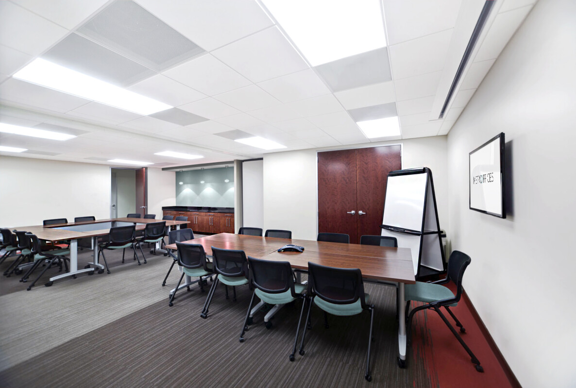 ?seraph accel gi=wp content%2Fuploads%2F2024%2F07%2F006 TR - Metro Offices A modern conference room with multiple tables, chairs, a presentation screen, a whiteboard, and a closed door in the background.
