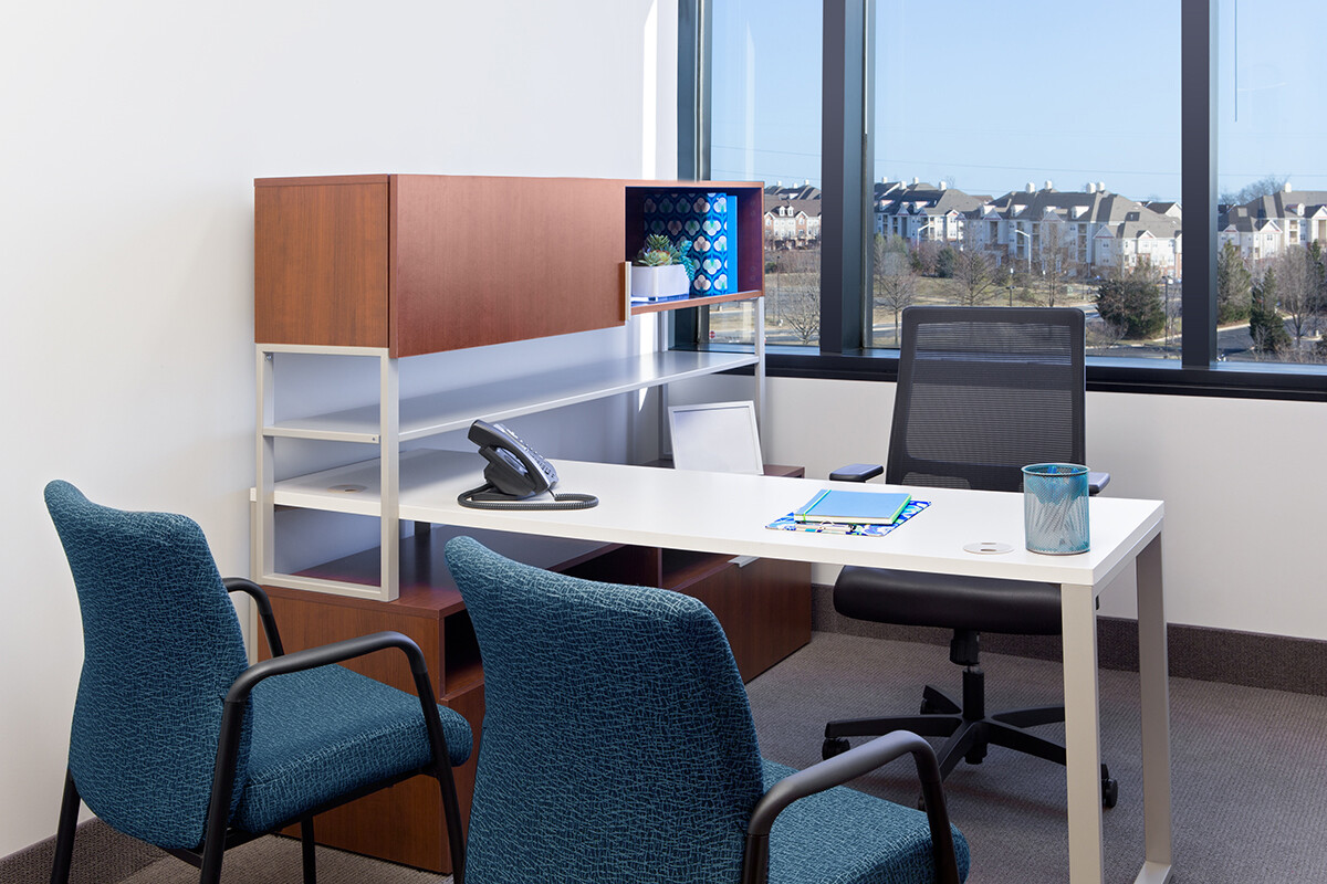 ?seraph accel gi=wp content%2Fuploads%2F2024%2F07%2F007 DO - Metro Offices Modern office with a desk, chair, telephone, notebook, pen, and a cup, flanked by two visitor chairs. A window offers a view of a cityscape and trees. Shelves and cabinets are visible behind the desk.