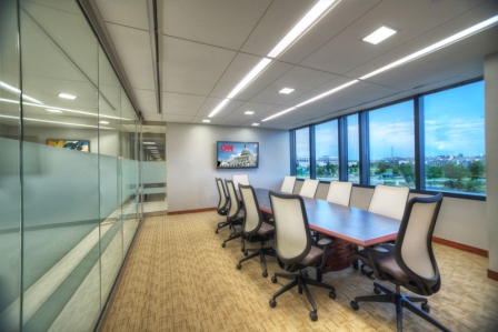 ?seraph accel gi=wp content%2Fuploads%2F2024%2F07%2FWoodland Sunrise - Metro Offices A modern conference room with a long table, surrounded by office chairs, a large window offering an exterior view, and a wall-mounted screen displaying a news channel.