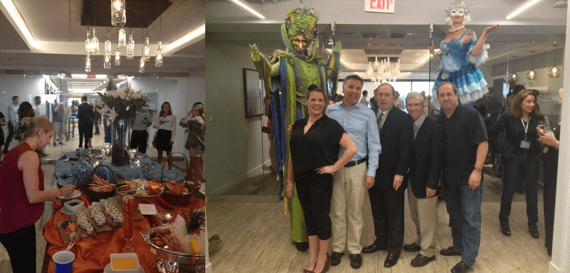 Metro Offices Debuts Progressive Shared Spaces at Grand Opening IMG2 - Metro Offices A group of people pose for a photo in an office hallway at Metro Offices' grand opening, next to performers on stilts, while others gather near a buffet table with food and drinks.