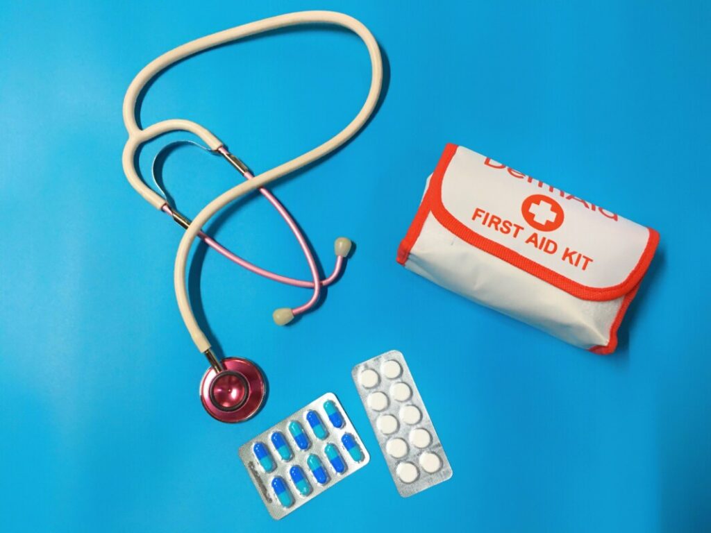 A first aid kit with a stethoscope and pills on a blue background in a workspace setting.
