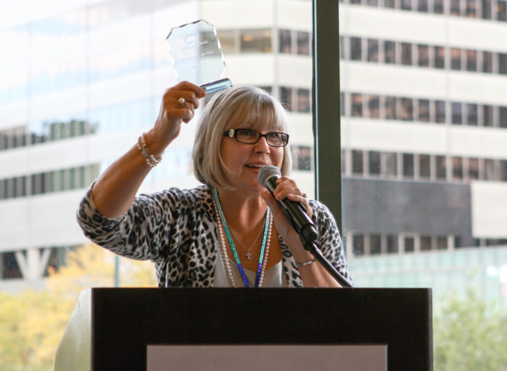 A woman speaking at a podium in Metro Offices and holding up an award.