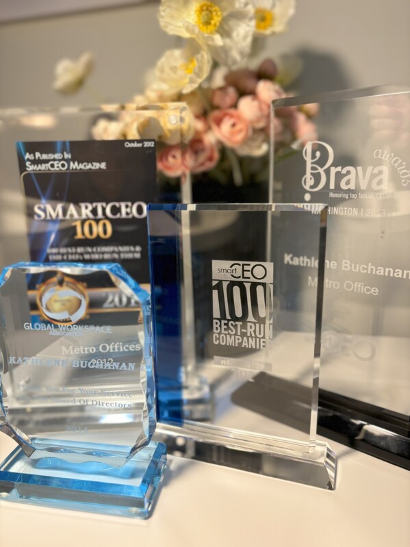 A collection of corporate awards from Metro Offices on display with a floral arrangement in the background, celebrating achievements under the leadership of Kathlene Buchanan.