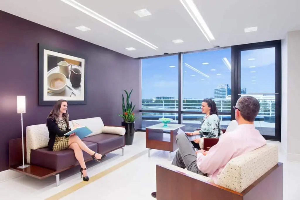 Three individuals having a meeting in a modern, private office space with a city view.
