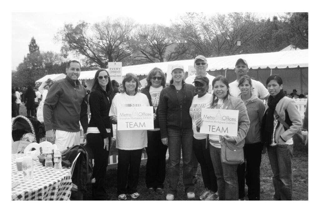 Group of people posing together with signs that say "Metro Offices team" at an outdoor event, including Kathlene Buchanan.